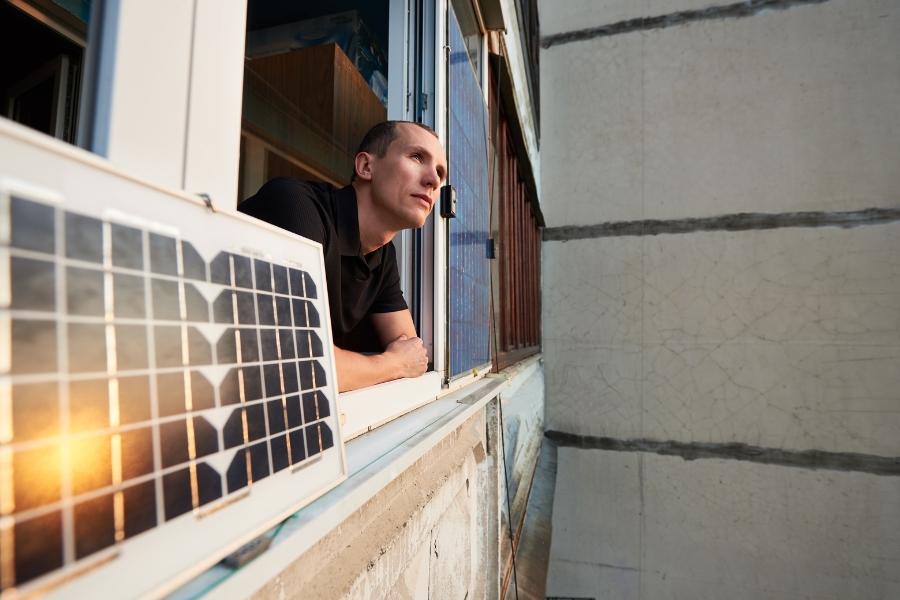 man looking out window beside balcony solar panel